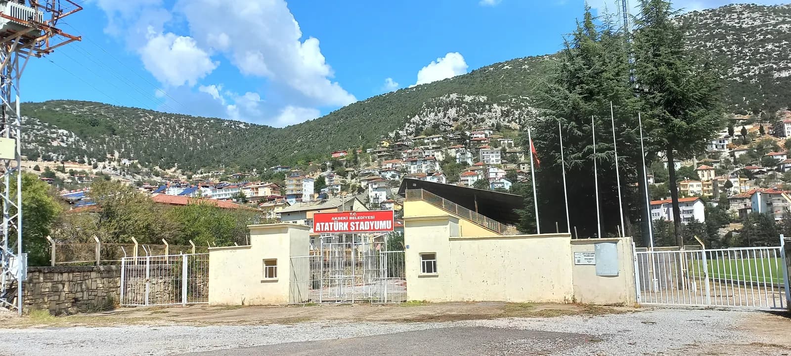 Akseki ilçe merkezi: çam ve sedir ağaçlarıyla kaplı yamaca yayılmış evler ve önde stadyum girişi