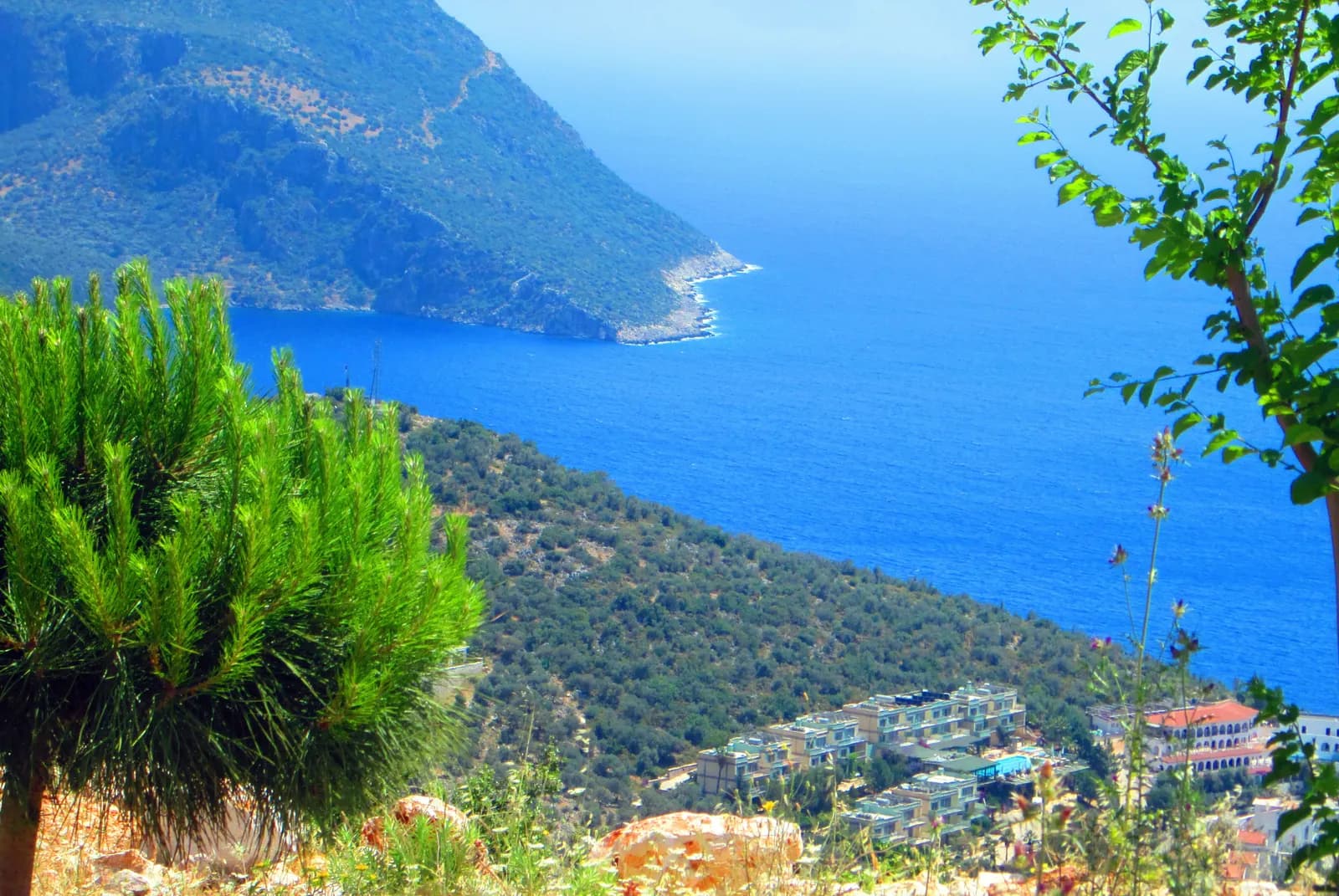 Kaş kıyısında berrak deniz, kayalık koy ve yamaçtaki yapılar