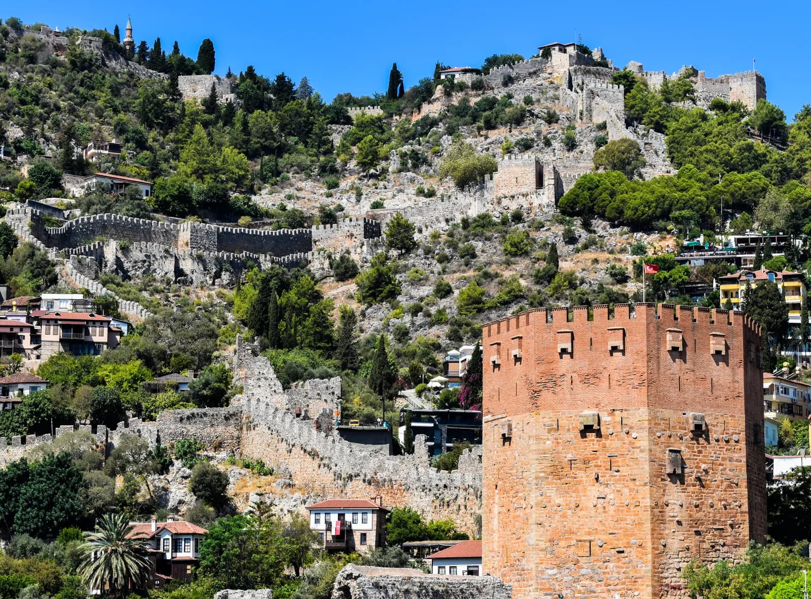 Alanya'da Kızıl Kule ve arkasında tepeye uzanan Alanya Kalesi surları