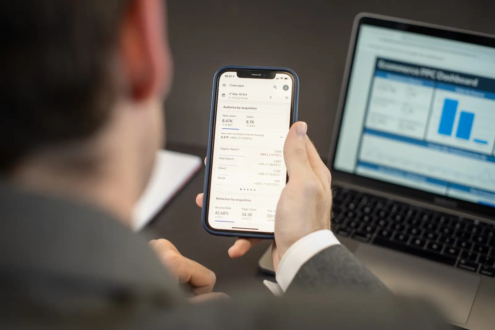 Elinde telefonla web sitesi trafik verilerine bakan bir kişi, arkada dizüstü bilgisayar